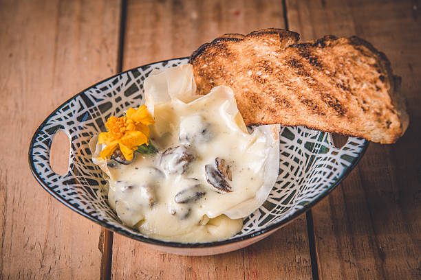 A gourmet dish featuring creamy mushroom sauce served in a decorative bowl, paired with toasted bread and garnished with a vibrant yellow flower. This rustic culinary presentation creates an inviting and appetizing scene, styled with rustic charm, making it ideal for representing elegant dining or food preparation concepts.