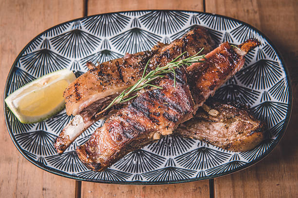 A close-up view of succulent grilled lamb ribs served on a beautifully patterned ceramic plate accompanied by a slice of lemon. Perfectly grilled with fresh herbs for garnish, the dish symbolizes gourmet dining and evokes indulgence in roasted meat dishes.