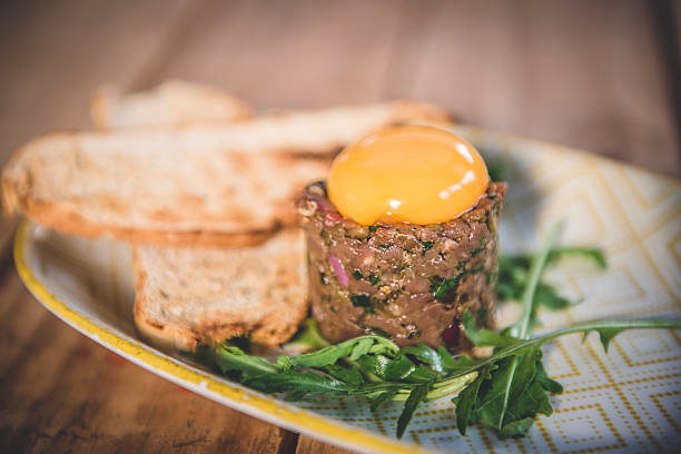Beef Tartare Served With Egg Yolk, Toast, and Arugula on a Plate