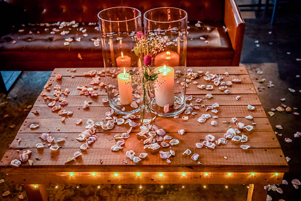 Beautifully arranged wooden table featuring rustic candles with soft lighting and scattered rose petals, evoking a romantic and cozy atmosphere. The warm tones and delicate floral ornamentation create a perfect ambiance for intimate celebrations or serene evenings.