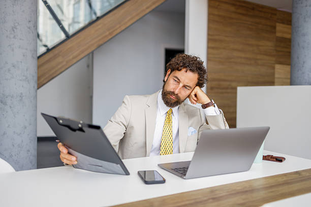 istock Tired businessman reading documents at office desk 2233996477