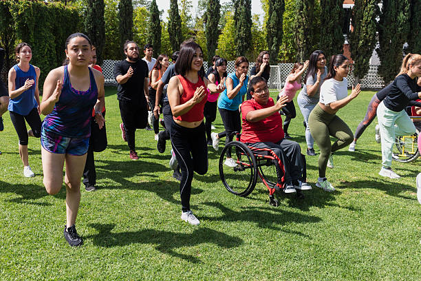 Large Group of Latin sporty multi age people stretching in training class next to mexican woman in wheelchair outdoors in a public park in Mexico Latin America. Diverse group in inclusion concept. stock photo