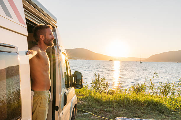 istock Man Standing in Camper Van at Lakeside Sunset 2234001635