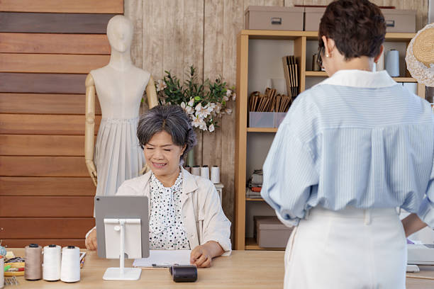 istock Senior asian tailor using tablet pos system while adult asian female client waiting after completing cashless payment inside boutique studio small fashion business checkout retail service 2234006947