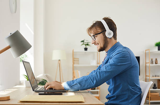 istock Young happy man in headphones typing on laptop and using internet web online services. 2234010638