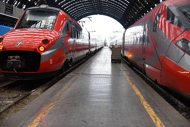 A train parked at the platform at the Milan, Italy train station.   Black and white.   High arch ceiling.