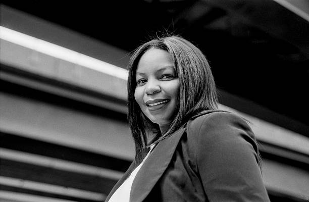 Grainy monochrome analog film photograph capturing a cheerful businesswoman smiling confidently under a bridge, taken with a vintage 35mm camera in an urban setting
