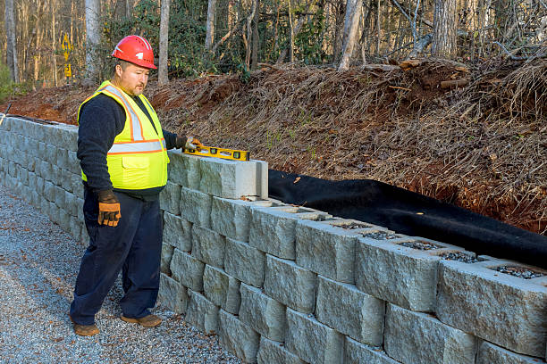 istock Construction worker checks alignment of retaining wall blocks near wooded area during daylight hours 2234015430
