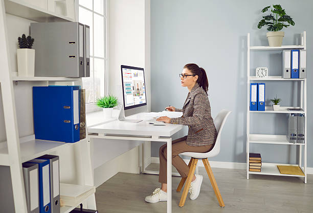istock Young woman working on a desktop computer at her desk in a modern office interior 2234015709