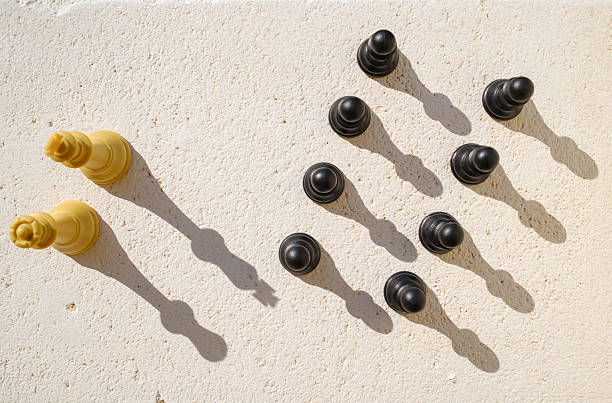 Two white king chess pieces are facing eight black pawn chess pieces on a concrete surface, casting long shadows in the bright sunlight, symbolizing a protest against racism