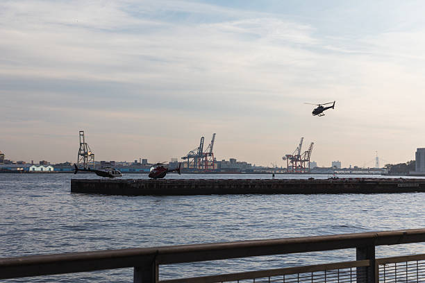 Helicopters hover and land near a waterfront pier with a scenic urban skyline, featuring industrial cranes and calm water, representing modern transportation, urban development, and waterfront activities.
