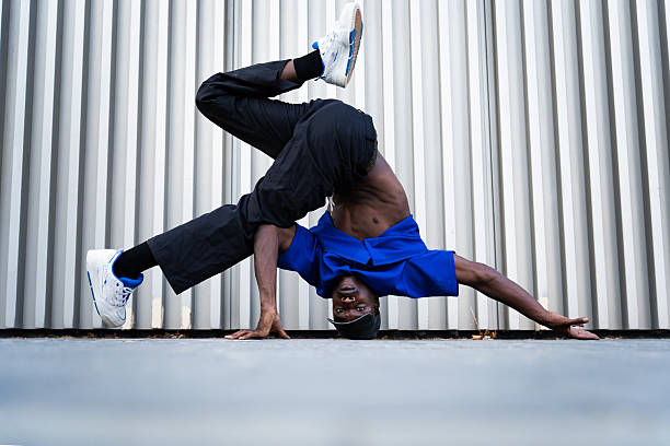 Breakdancing performer balancing upside down, head spinning near metallic urban backdrop, demonstrating street dance prowess and dynamic movement