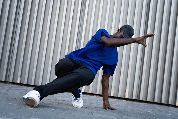 istock Male breakdancer performing dynamic street move, wearing blue shirt and backwards cap against gritty urban backdrop 2234019877