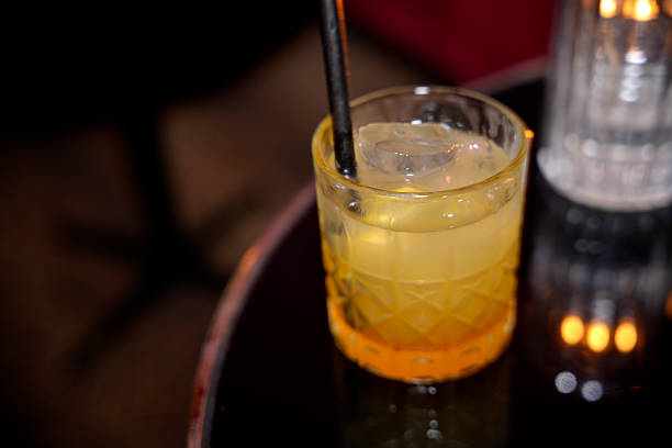 istock Refreshing yellow cocktail glowing on table in dark bar with ice and straw 2234023415