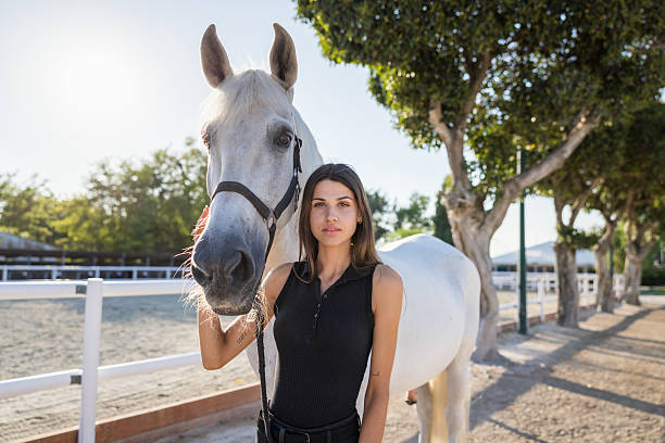 Young woman gently caressing her white horse in a riding school at sunset, embodying a profound bond between human and animal, radiating love and tranquility
