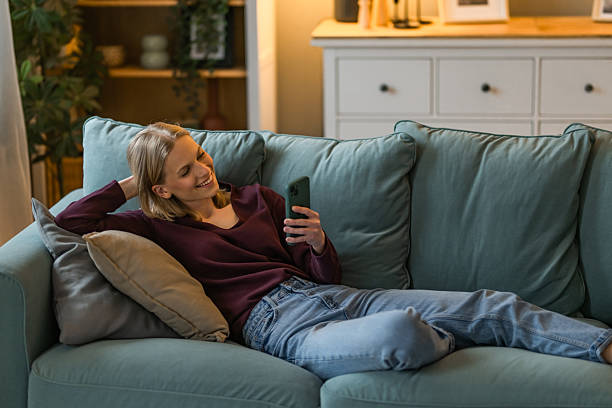 istock Young woman using phone while relaxing on sofa at home. 2234028376
