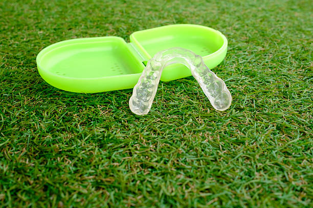 Transparent dental splint for bruxism or teeth whitening placed near its green carrying case, both lying on a synthetic grass surface, representing oral care and outdoor activities