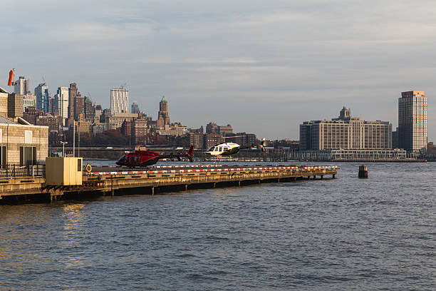View of a city skyline with skyscrapers and a helicopter on a waterfront heliport.