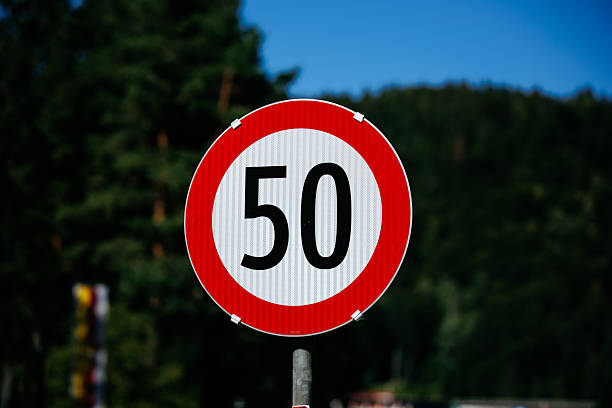 Speed limit sign with 50 in red circle against green forest background, lifestyle