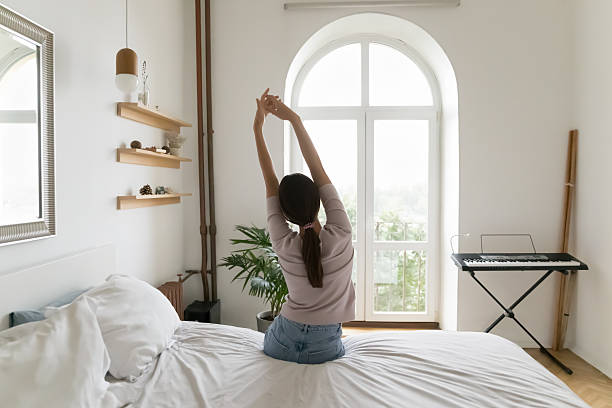 istock Rear view young woman stretch arms sitting on bed edge 2234044399