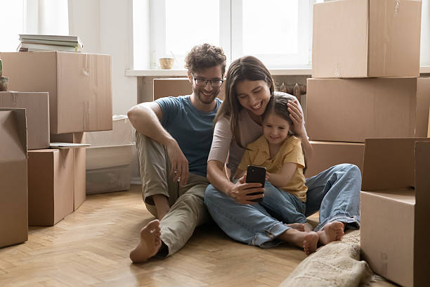 istock Happy couple with daughter using phone on floor among boxes 2234044630