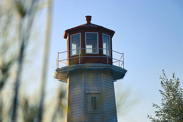 Close-up view of a classic red and white lighthouse tower with balcony and windows, photographed under a clear summer sky. Symbol of guidance, direction, and coastal navigation.