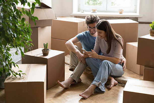 istock Happy couple sitting on floor among moving boxes using phone 2234050535