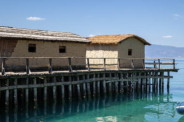 istock a rustic stilt village on a tranquil lake with traditional mud huts and thatched roofs. the wooden pier reflects in the clear turquoise water against a backdrop of distant mountains 2234052287