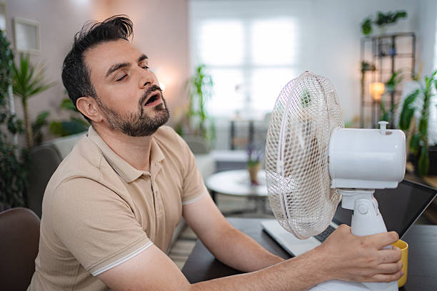 istock Overheated man cooling off with electric fan at home 2234053694