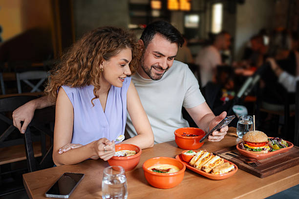 istock Happy couple looking at smartphone and eating in restaurant 2234055954