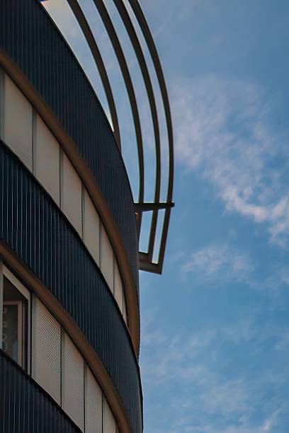 A sleek modern building with a curved design is partially silhouetted against a vibrant sky filled with soft clouds. The interplay of structure and nature creates a visually compelling contrast, perfect for themes of design, and urban aesthetics.