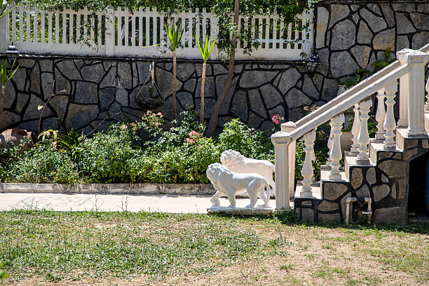 a narrow flower bed along the driveway to the house made of light beige ceramic tiles. boulders softened by water with pebbles, a bed filled with pebbles