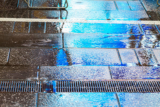Rain falling on a New York City sidewalk creates shimmering puddles, reflecting vibrant blue neon lights from Times Square during a rainy autumn night in the urban landscape