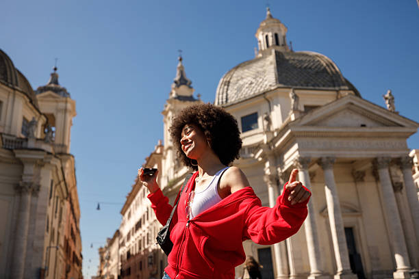 Young woman dancing joyfully while listening to music on her phone at Piazza del Popolo in Rome.