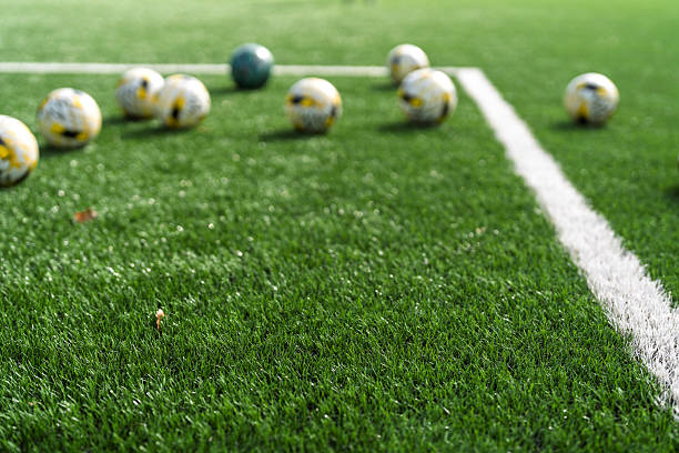 Close-up of soccer balls scattered on green artificial turf near a white field marking line.