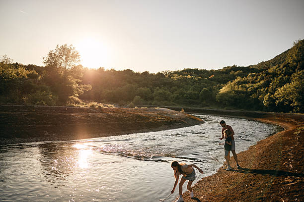 Single father is playing with his children on a river. It’s a beautiful sunset.