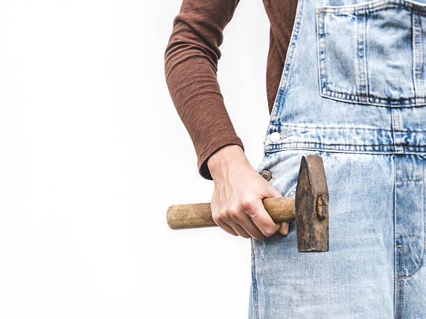 Cute woman, work clothes and hammer. Labor day. Close-up, indoors. Studio shot. Front view, close-up. Labor and employment concept
