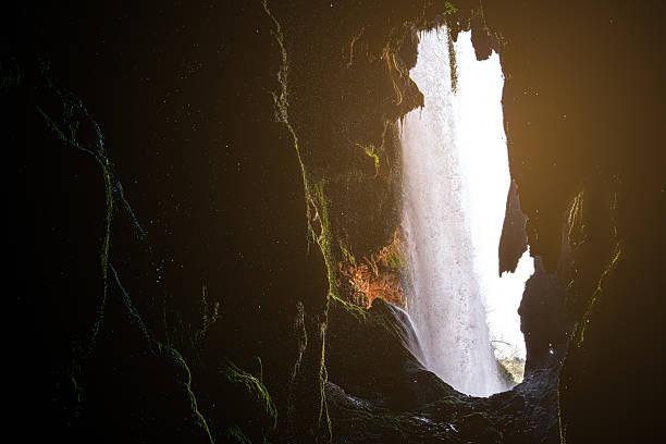Bright sunlight illuminating waterfall flowing from rocky cliff inside dark mossy cave at monasterio de piedra natural park, nuevalos, spain