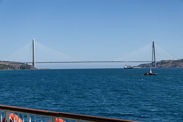 Istanbul, Turkey - September 7, 2025: Scenic view of the Yavuz Sultan Selim Bridge spanning the Bosphorus, photographed from the deck of a ferry with orange lifebuoys along the railing under a clear blue sky.