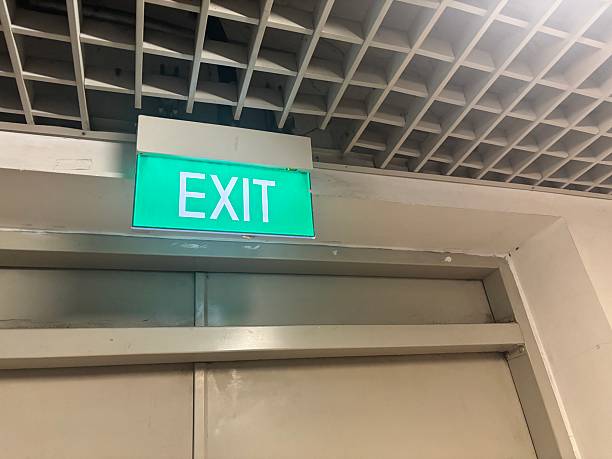 istock Illuminated green exit sign above a doorway with a square ceiling grid above providing guidance during emergencies or fire incidents in commercial buildings safety equipment direction 2234098516