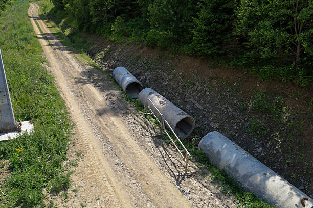 istock A dirt road winding through a forested slope highlights a path to a remote area. Pipes left along the roadside create a sense of ongoing construction, and the green forest adds contrast to the abandoned objects. 2234101673