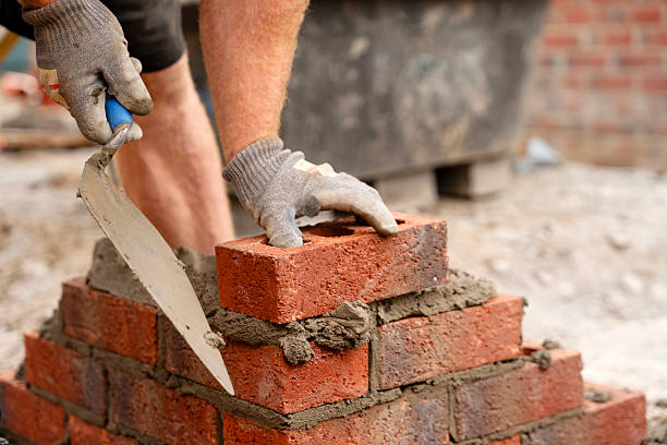 istock Skilled mason laying red bricks with mortar at construction site in sunny weather, showcasing craftsmanship and focus on detail during brickwork activity 2234102168