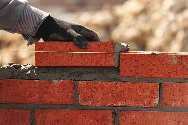 istock Skilled worker laying red bricks in a construction site during daylight with focused attention on building a wall 2234105416