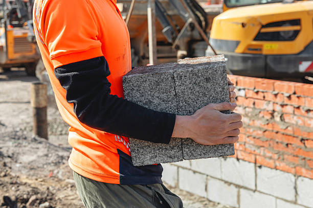 istock Construction worker carries concrete block on a building site in a sunny afternoon while machinery operates in the background near completed brick wall 2234105545