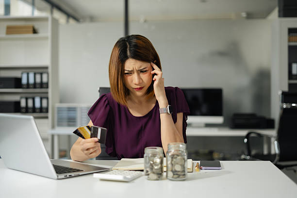 Asian woman stressed over credit card debt, holding bills in frustration. stock photo