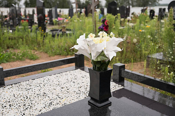 Close view of a shiny black gravestone with no name and a lantern and vibrant red and white flowers in front