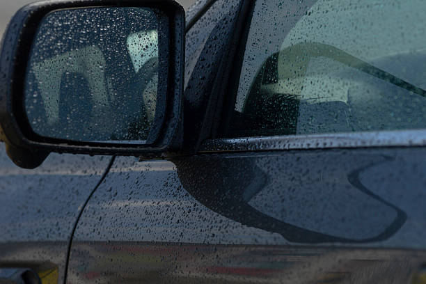 A close-up shot of a car's side mirror and door, adorned with raindrops, capturing the essence of a rainy day.