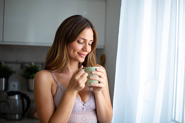 istock Smiling woman drinking coffee by the window in her kitchen 2234114260