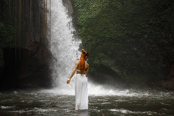 istock Woman standing by a waterfall surrounded by lush greenery in serene nature 2234126114