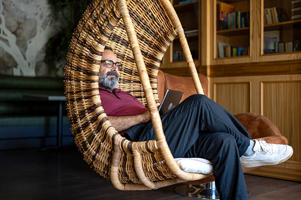 Bearded man sitting on wicker swing manages his business with computer.